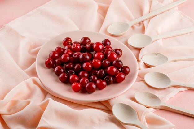 Cerises dans une assiette avec des cuillères en bois high angle view on textile et rose