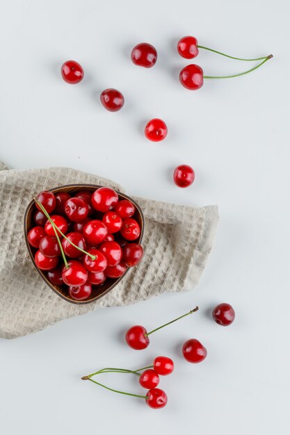 Photo gratuite cerises dans un bol sur blanc et torchon.