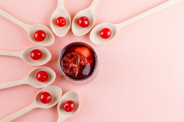 Cerises dans des cuillères en bois avec boisson glacée à plat sur un espace rose