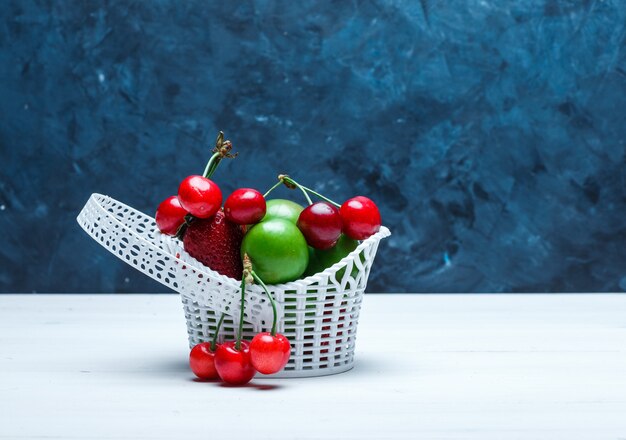 Cerises dans un panier avec fraises et prunes vertes