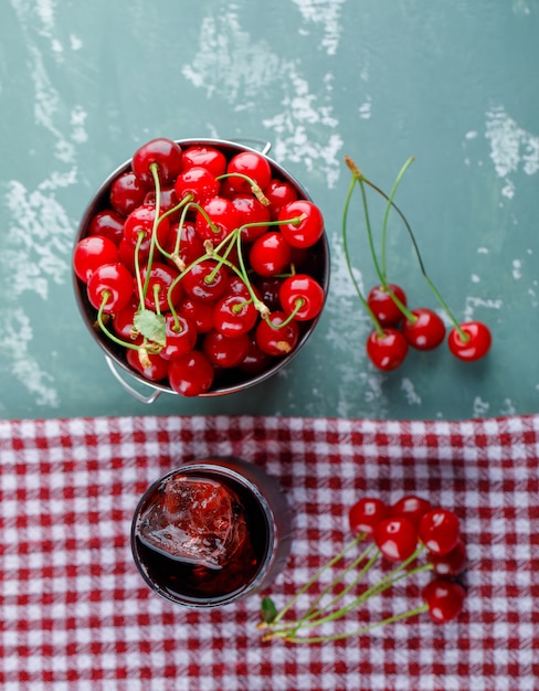 Photo gratuite cerises dans un seau avec vue de dessus de jus sur plâtre et torchon