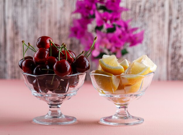 Cerises dans un vase avec des tranches de citron, vue latérale du pot de fleur sur la surface rose et grungy