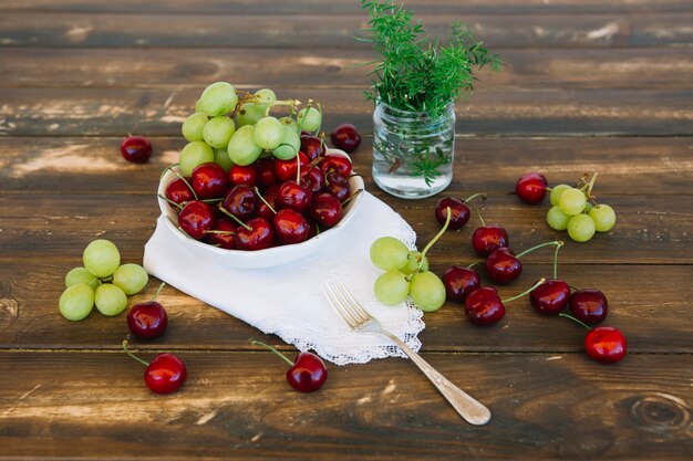 Cerises fraîches et raisins dans un bol sur fond de bois