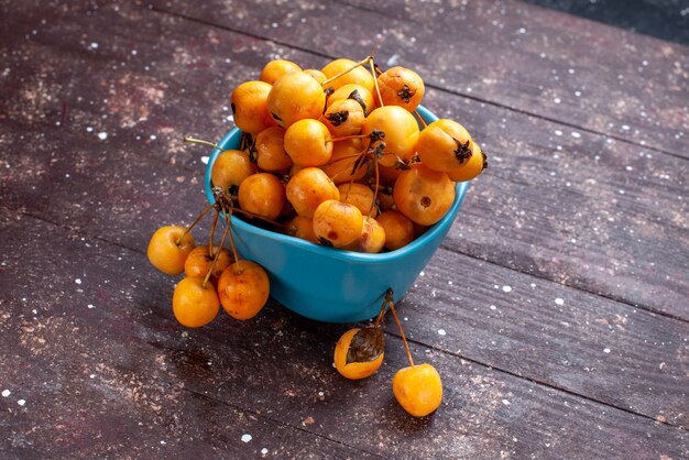 Cerises jaunes moelleuses fraîches et mûres à l'intérieur d'un bol bleu sur brown