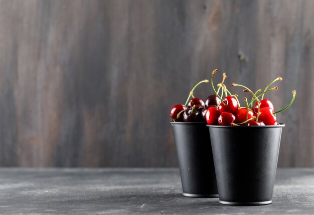 Cerises en mini seaux vue latérale sur grunge et surface grise