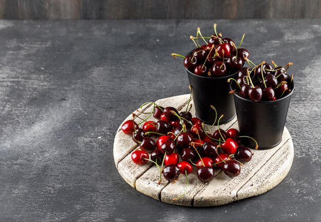 Cerises avec planche de bois dans des seaux sur une surface grungy et en bois, vue grand angle.