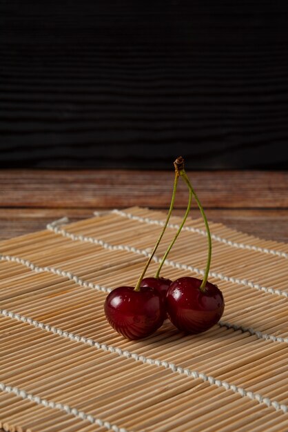 Cerises rouges avec des tiges vertes sur le mat rustique