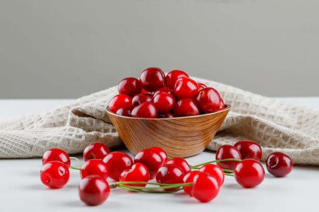 Cerises avec torchon dans un bol sur blanc et gris