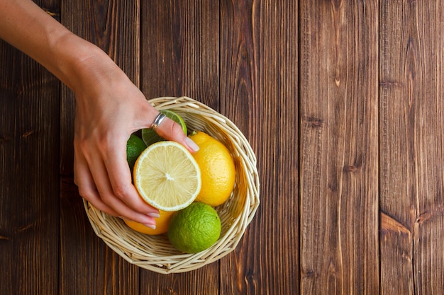 Certains citrons avec main tenant la moitié du citron dans un panier sur fond de bois, vue du dessus.