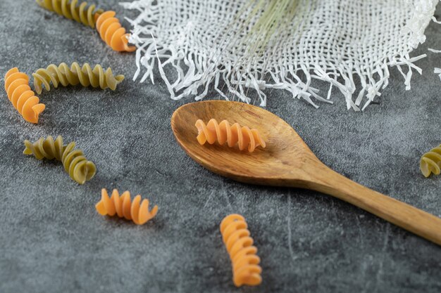 Certains des macaronis crus en spirale colorés avec une cuillère en bois