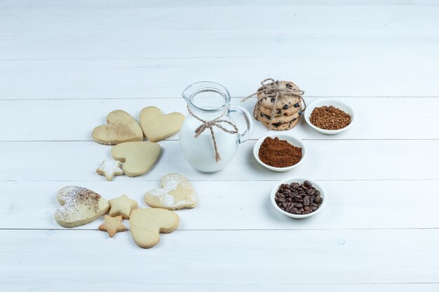 Certains types de biscuits avec grains de café, café instantané, cacao, cruche de lait sur fond de planche de bois blanc, vue grand angle.