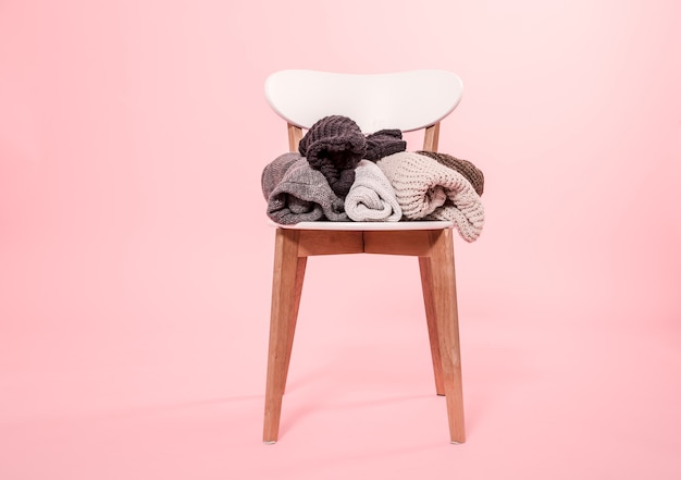 Photo gratuite chaise blanche avec une pile de pulls tricotés sur fond rose