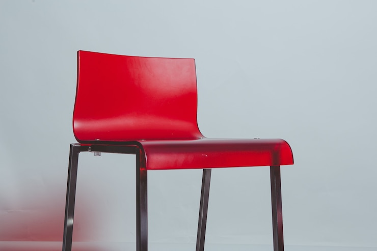 Une chaise en plastique rouge sur un mur blanc.