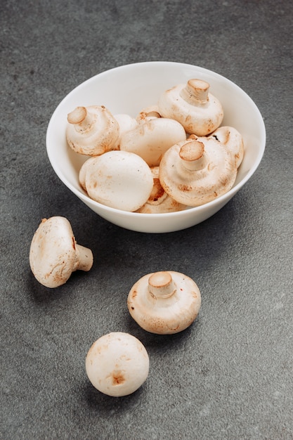 Champignons blancs dans un bol sur un fond texturé gris. vue grand angle.