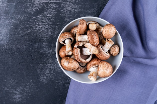 Champignons dans un bol sur un tissu violet sur une table sombre