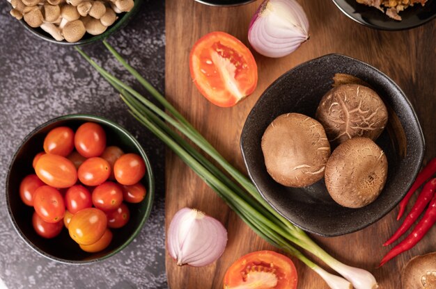 Champignons shiitake à l'ail, tomate, poivron, oignon nouveau et oignons rouges sur un sol en ciment noir.