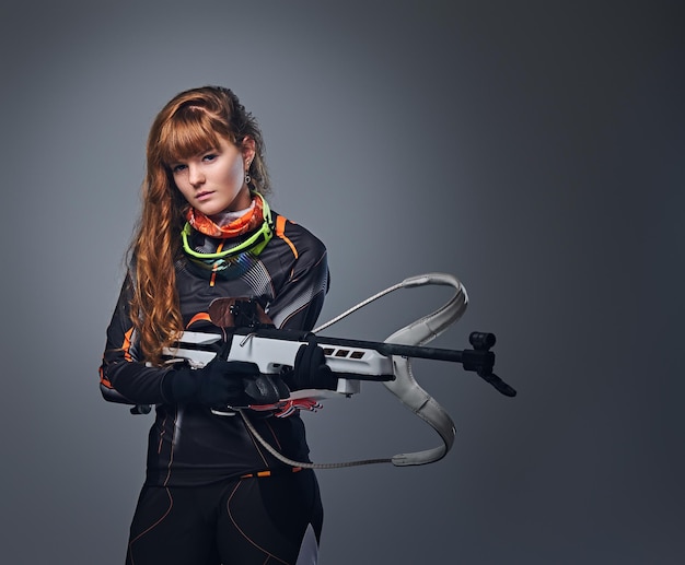 Photo gratuite championne de biathlon rousse visant avec une arme de compétition dans un studio sur fond gris. championne de biathlon rousse visant avec une arme de compétition dans un studio sur fond gris.