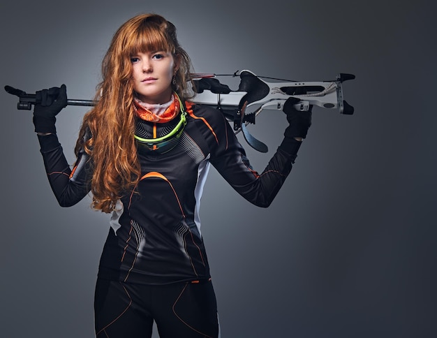 Championne de biathlon rousse visant avec une arme de compétition dans un studio sur fond gris. Championne de biathlon rousse visant avec une arme de compétition dans un studio sur fond gris.