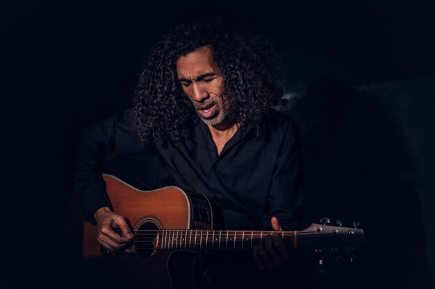 Le chanteur de rock charismatique pose avec sa guitare en chantant dans un studio sombre.