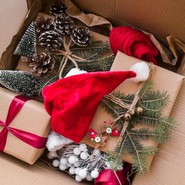 Chapeau de Noël près de boîtes-cadeaux décorées de brindilles de sapin dans une boîte en carton