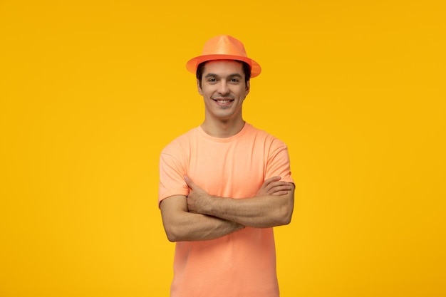 Chapeau orange jeune mec mignon souriant avec les mains croisées en tshirt orange