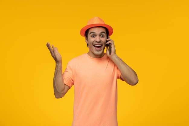 Chapeau orange mignon jeune homme en t-shirt orange avec le chapeau parlant au téléphone et riant