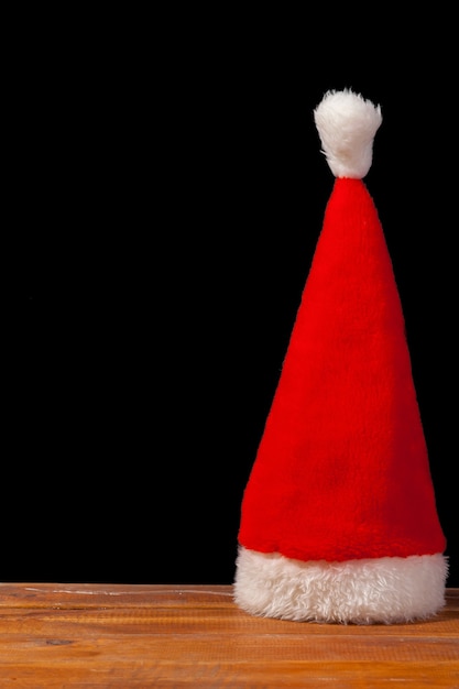 Photo gratuite le chapeau de santa rouge sur table en bois sur fond noir