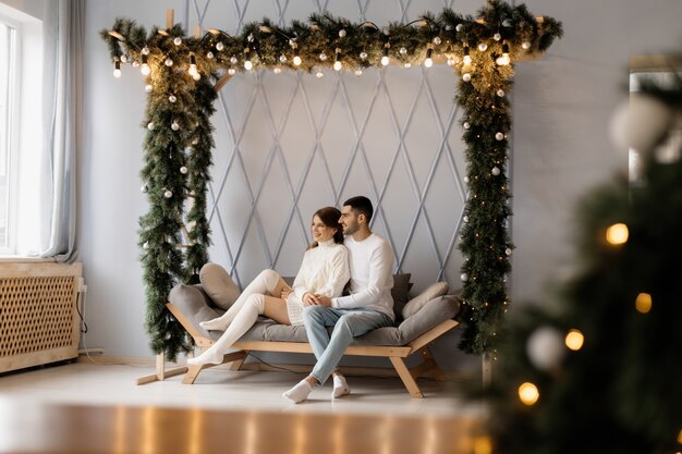 Charmant jeune couple en vêtements de maison blancs confortables pose dans une chambre avec arbre de Noël