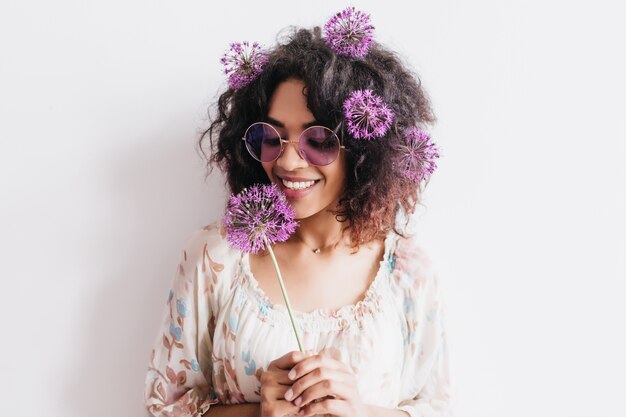 Charmant modèle féminin à la peau foncée tenant allium et exprimant le bonheur. Photo intérieure d'une femme élégante avec une fleur.