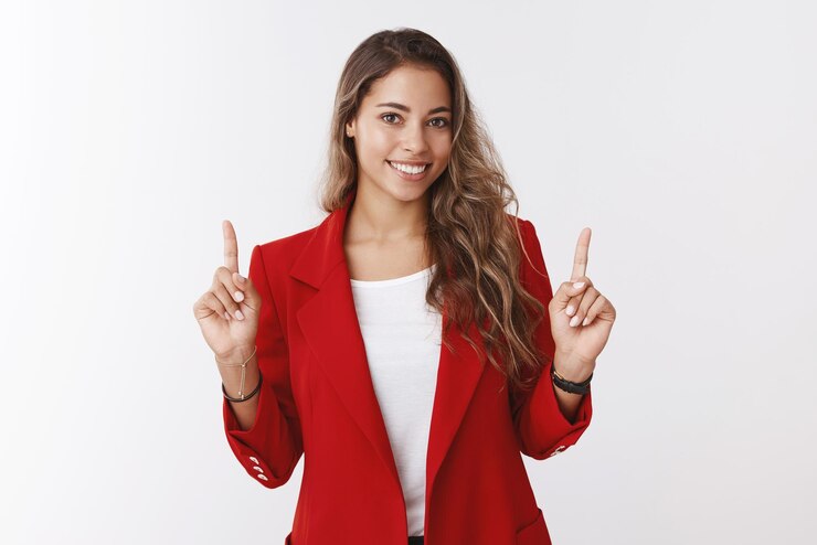 Photo gratuit charmante créative souriante heureuse assistante de bureau montrant au client un espace de copie parfait levant les index pointant vers le haut souriant confiant caméra amicale portant une veste à la mode rouge