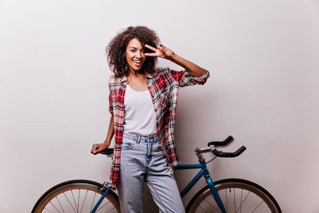 Charmante cycliste en chemise à carreaux en riant. Femme de bonne humeur posant avec vélo et exprimant son bonheur.