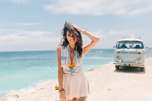 Charmante femme adorable habillée avec une chemise en jean et une jupe profite de ses vacances sur la plage