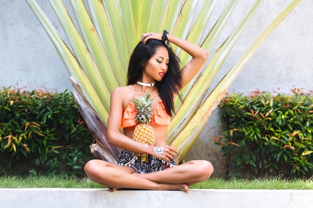 Charmante femme assise en posture de lotus et tenant ananas