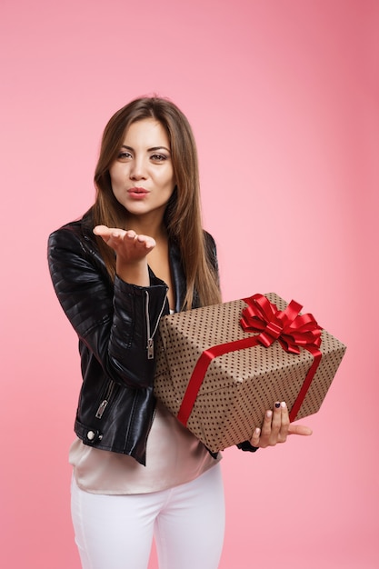 Charmante femme aux cheveux longs souffle baiser en regardant droit, tenant présent