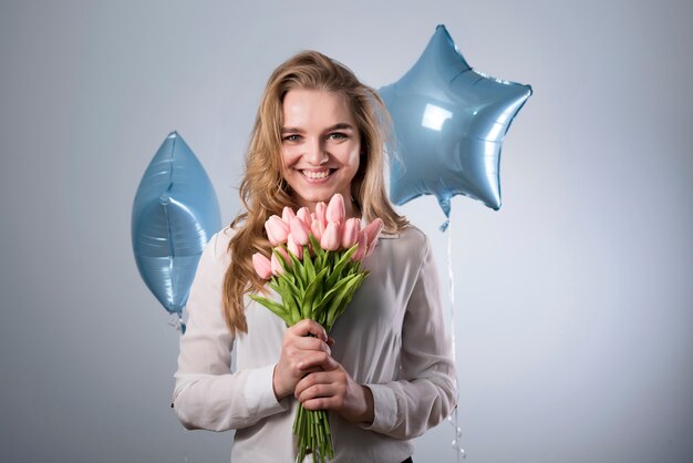 Charmante femme heureuse avec bouquet de fleurs et ballons
