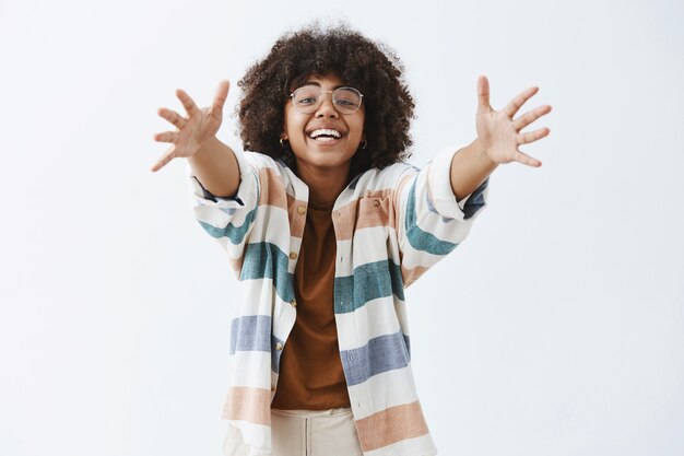 Charmante femme moderne afro-américaine amicale et mignonne en tenue élégante tirant les mains vers pour donner un câlin