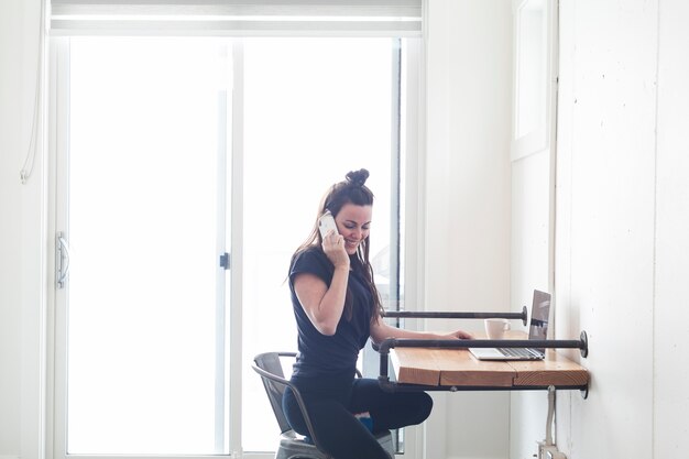 Charmante femme parlant au téléphone à table