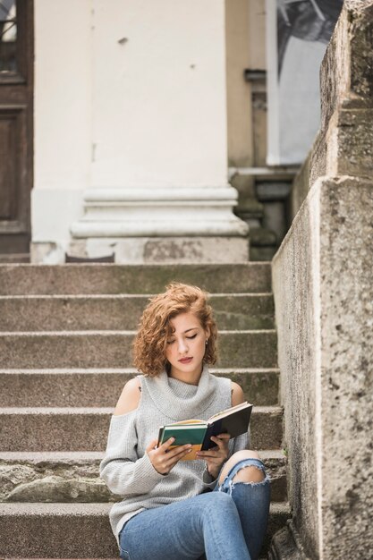 Charmante femme avec un petit livre de lecture de cheveux bouclés