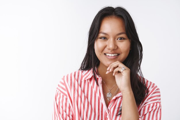 Charmante femme vietnamienne avec tatouage écoutant avec enthousiasme et joie ayant une conversation intéressante touchant la lèvre de curiosité souriant largement posant intrigué sur fond blanc