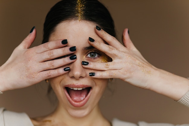 Photo gratuite charmante fille aux cheveux noirs posant avec un sourire surpris. jolie jeune femme aux cheveux noirs en riant