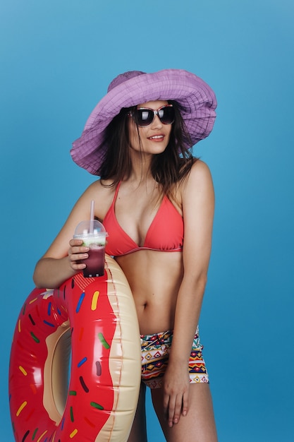 Charmante fille en chapeau et robe de plage avec un anneau de bain cocktail et beignet