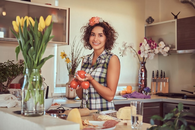 La charmante fille hispanique bouclée tient des tomates fraîches pendant la cuisson dans sa cuisine.