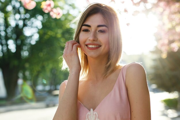 Charmante jeune femme en robe rose pose devant un arbre de sakura plein de fleurs roses