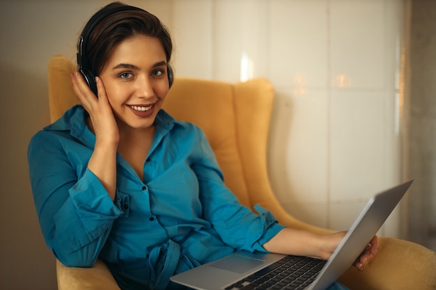 Photo gratuite charmante jeune femme travaillant à distance sur un ordinateur portable, écoutant de la musique via des écouteurs sans fil