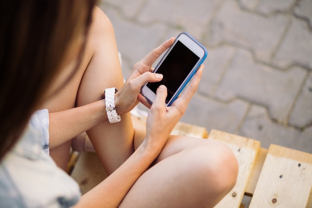 Charmante jeune fille assise sur une palette à l'aide de téléphone intelligent