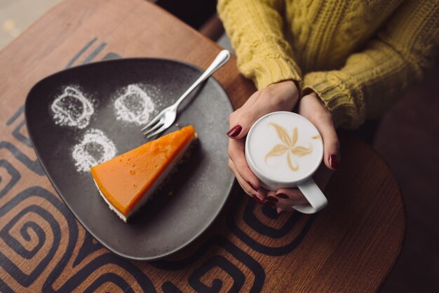 Charmante jeune fille buvant un cappuccino et mangeant un cheesecake