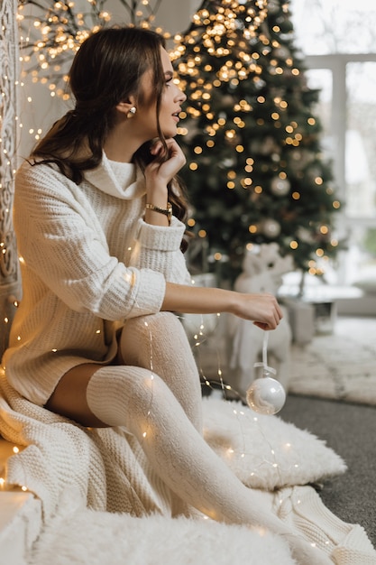 Charmante jeune fille dans une robe tricotée détient un jouet de Noël et regarde de côté