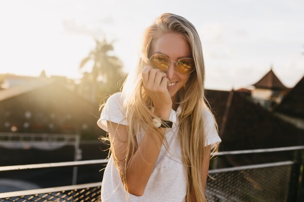 Charmante jeune fille en montre-bracelet posant avec un sourire timide sur fond de ciel.