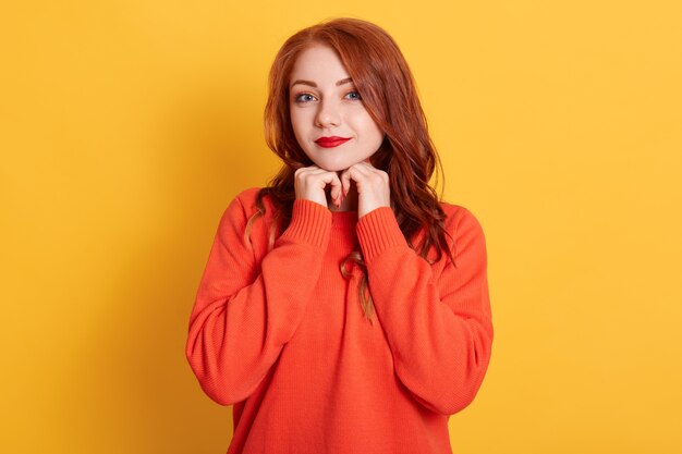 Charmante jolie jeune femme aux cheveux roux avec une expression mignonne, regardant la caméra, souriant joyeusement, se sentant détendue et heureuse