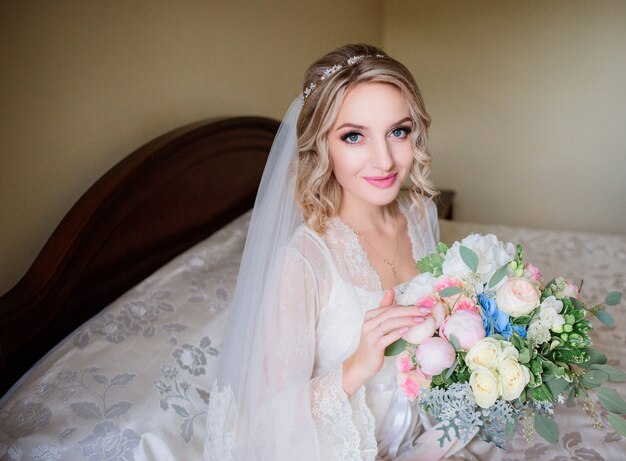 Charmante mariée dans une robe blanche s&#39;assied avec bouquet de mariage sur la table du dîner